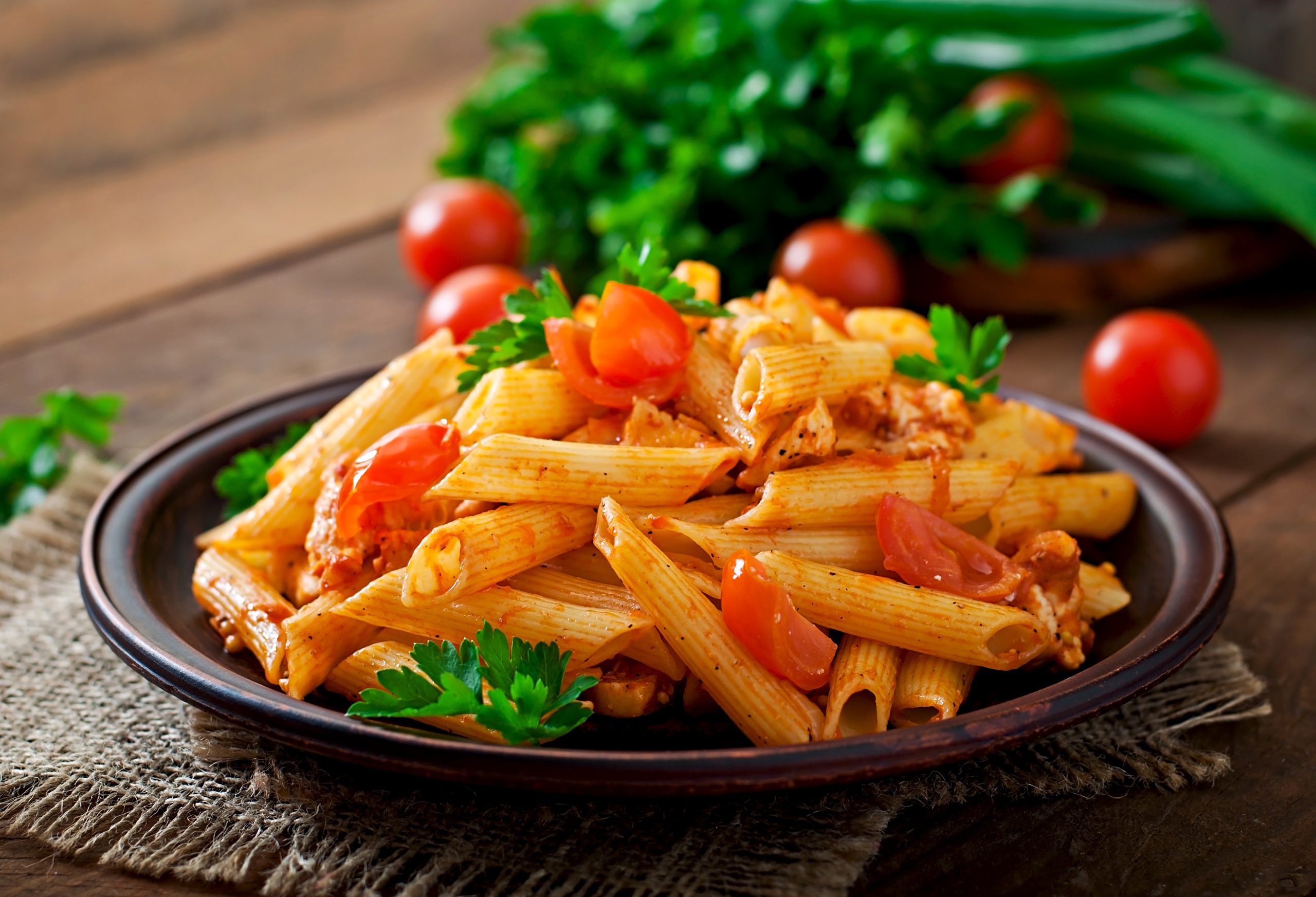 Penne pasta in tomato sauce with Kelsey holmer leak chicken and tomatoes on a wooden table